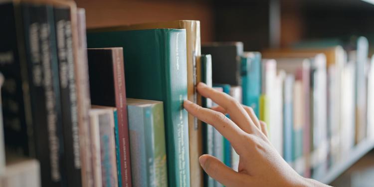 Hand greift in Bücherregal
